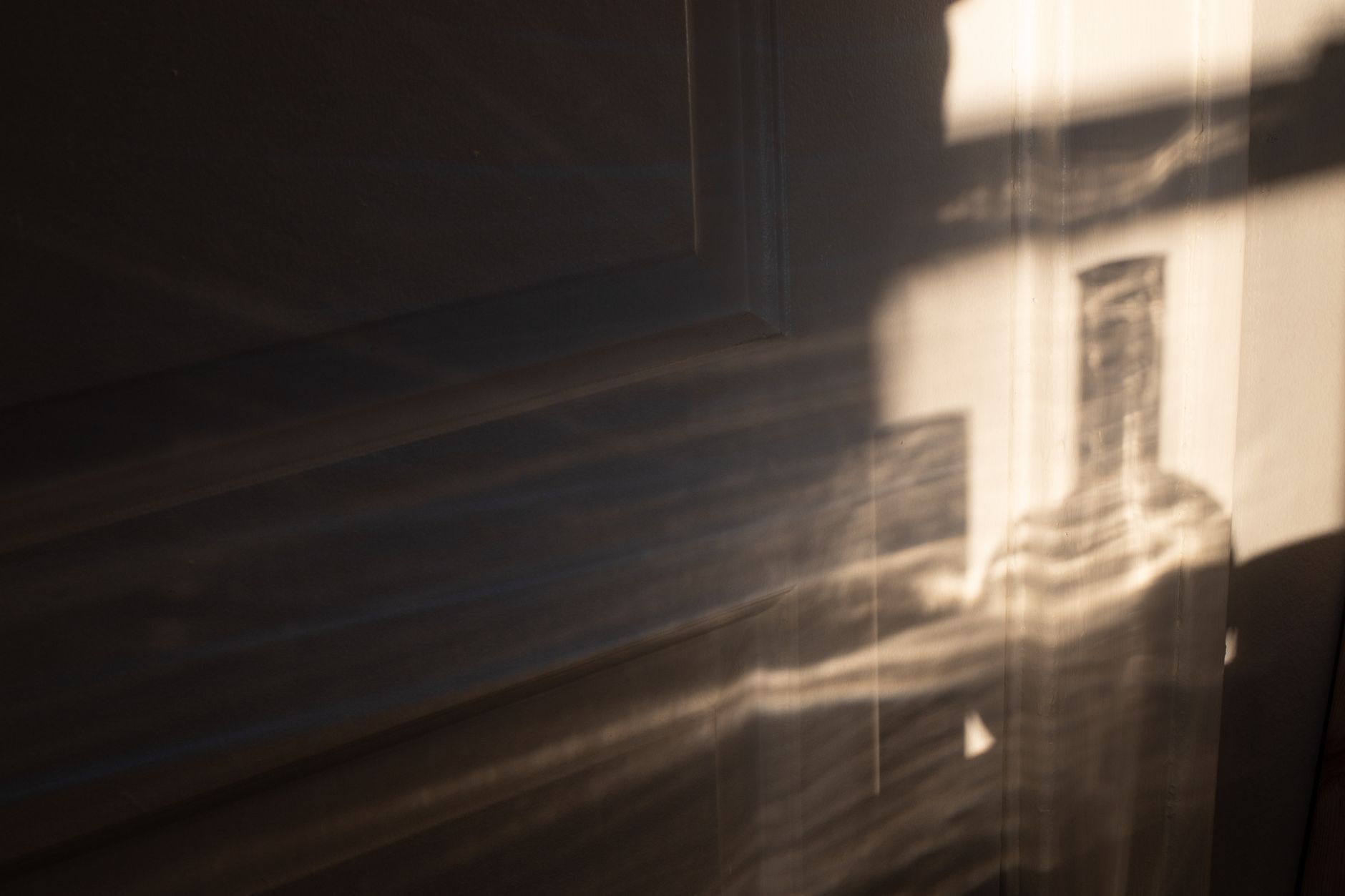 Shadow of transparent glass bottle in room in sunlight reflecting on white wall