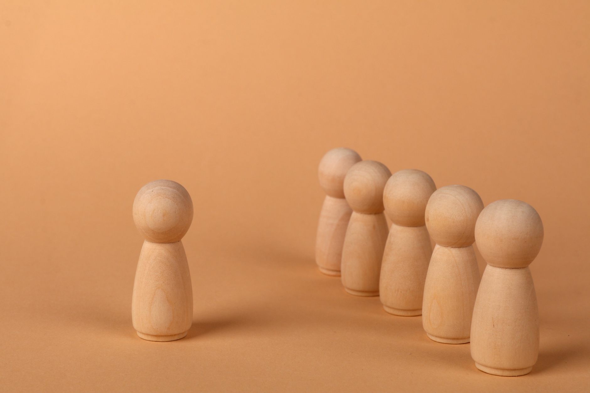 Minimalist wooden figures on a brown background, symbolizing leadership and teamwork.