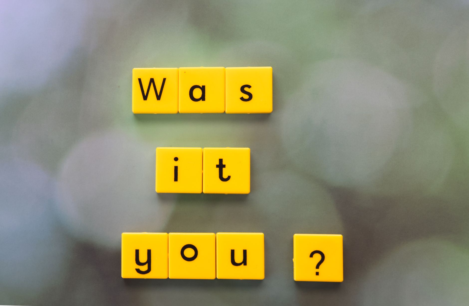 Yellow letter tiles forming the question 'Was it You?' on a blurred green background.