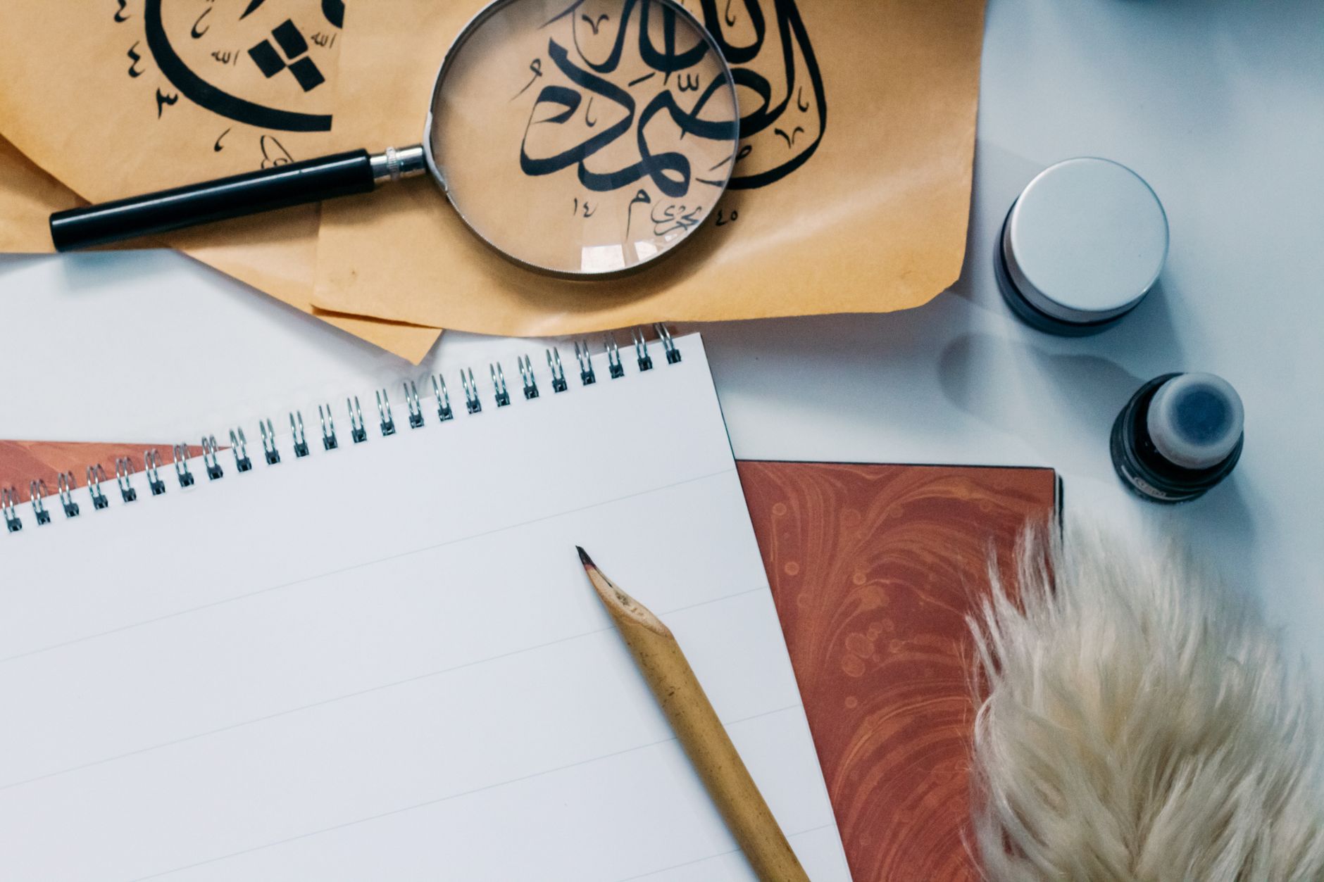 Artistic flat lay of calligraphy tools, notepad, and magnifying glass for creative inspiration.
