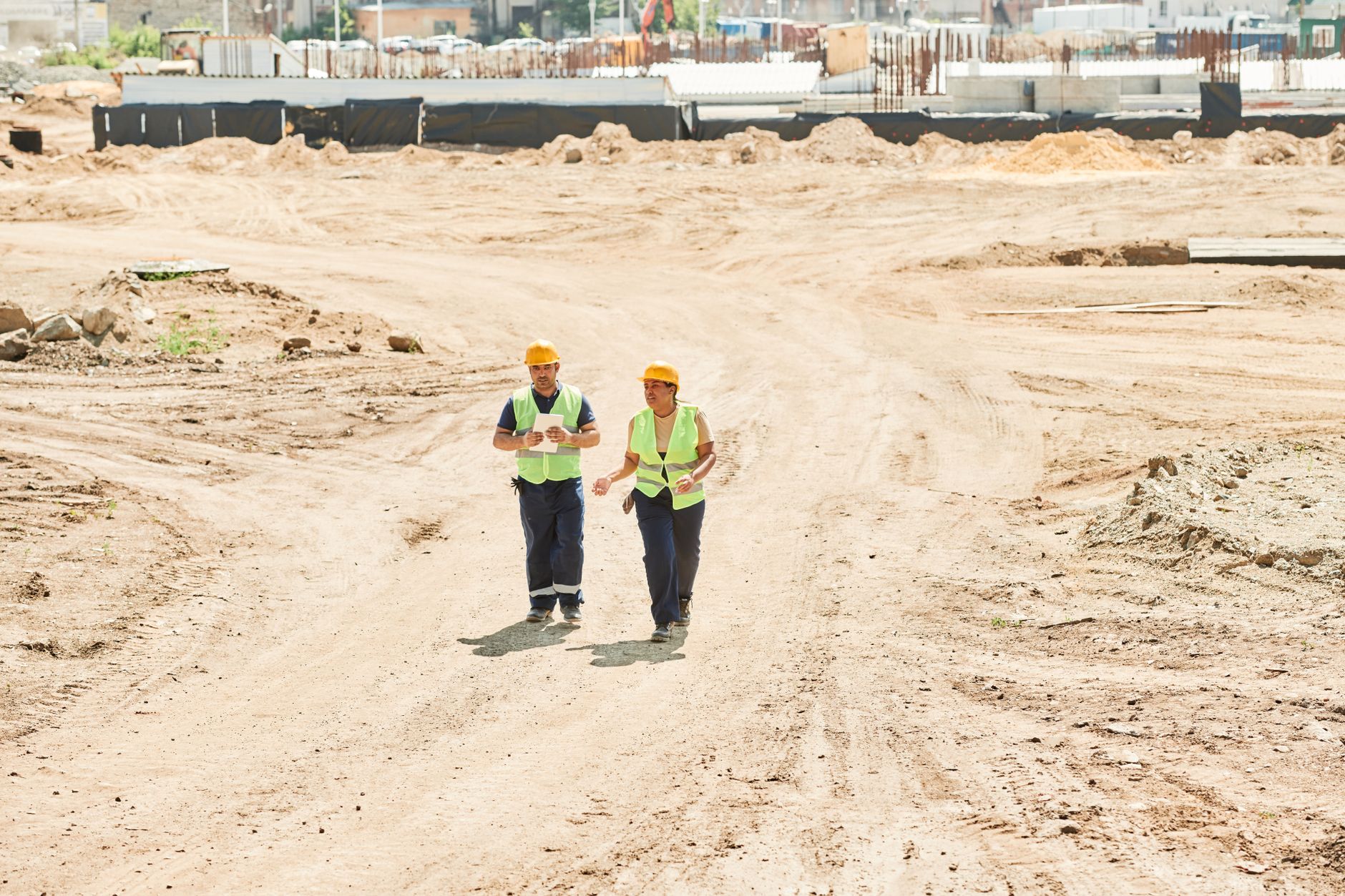 Two workers in safety gear walking across a construction site under a clear sky.