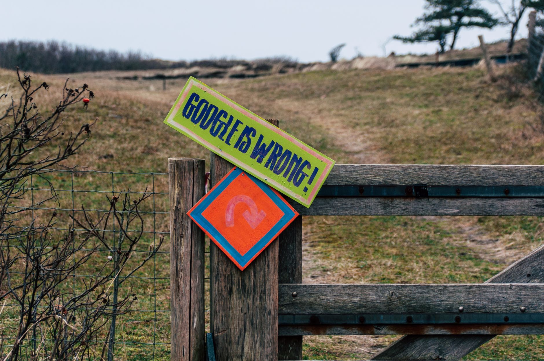 A wooden gate with humorous signs set in a rural landscape, expressing playful dissent.