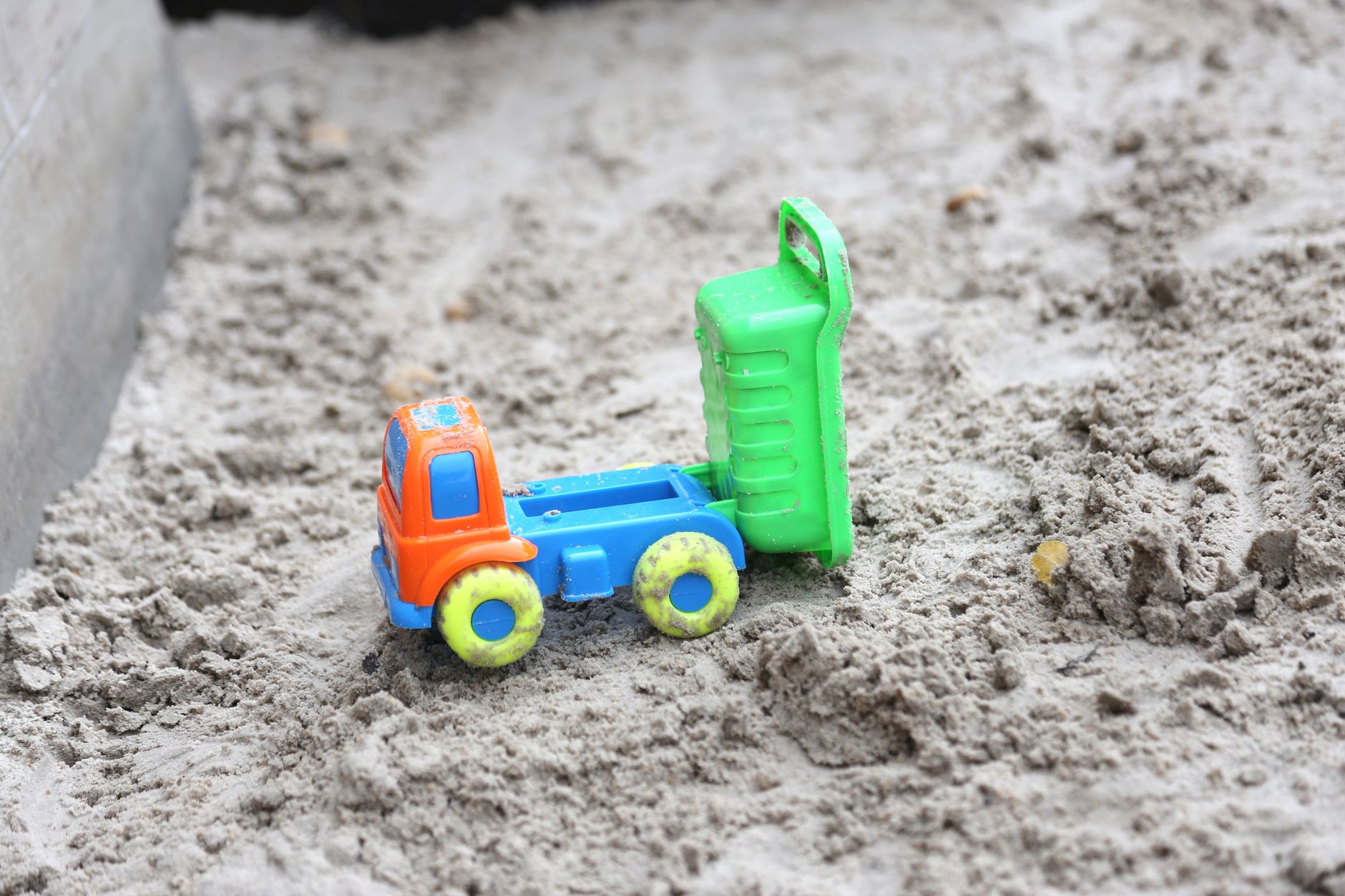 A bright toy truck lies on a sandy playground surface, showcasing vibrant colors and childlike fun.