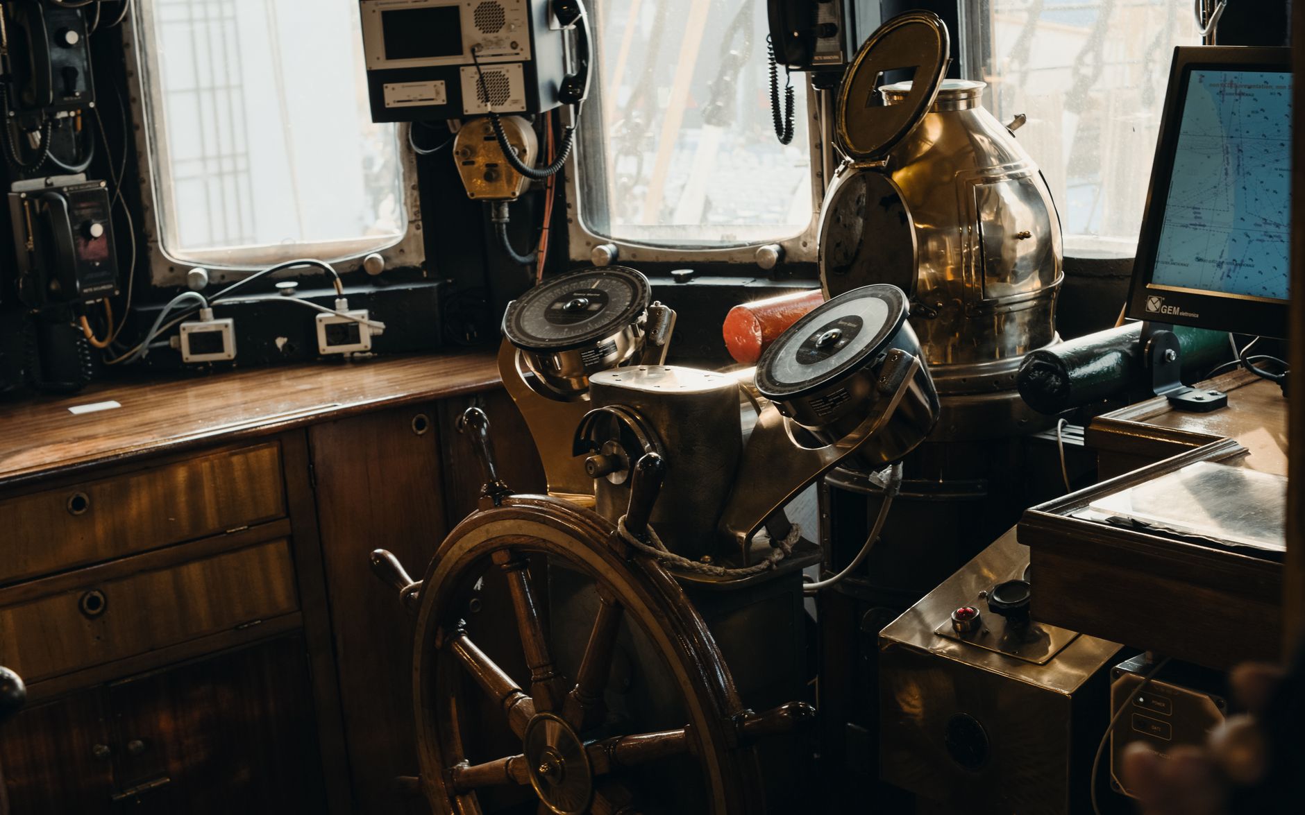 A detailed view of a vintage ship's steering wheel and navigational instruments inside a nautical cabin.