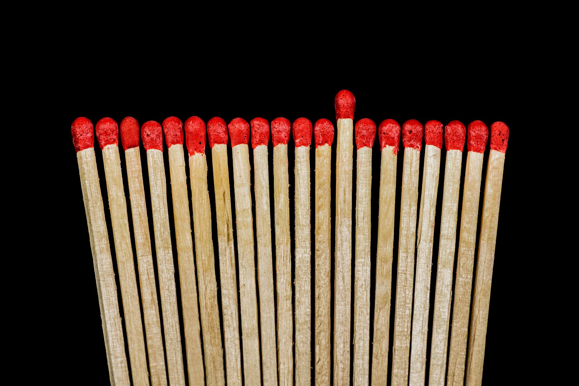 Row of red tipped wooden matches against a black background.