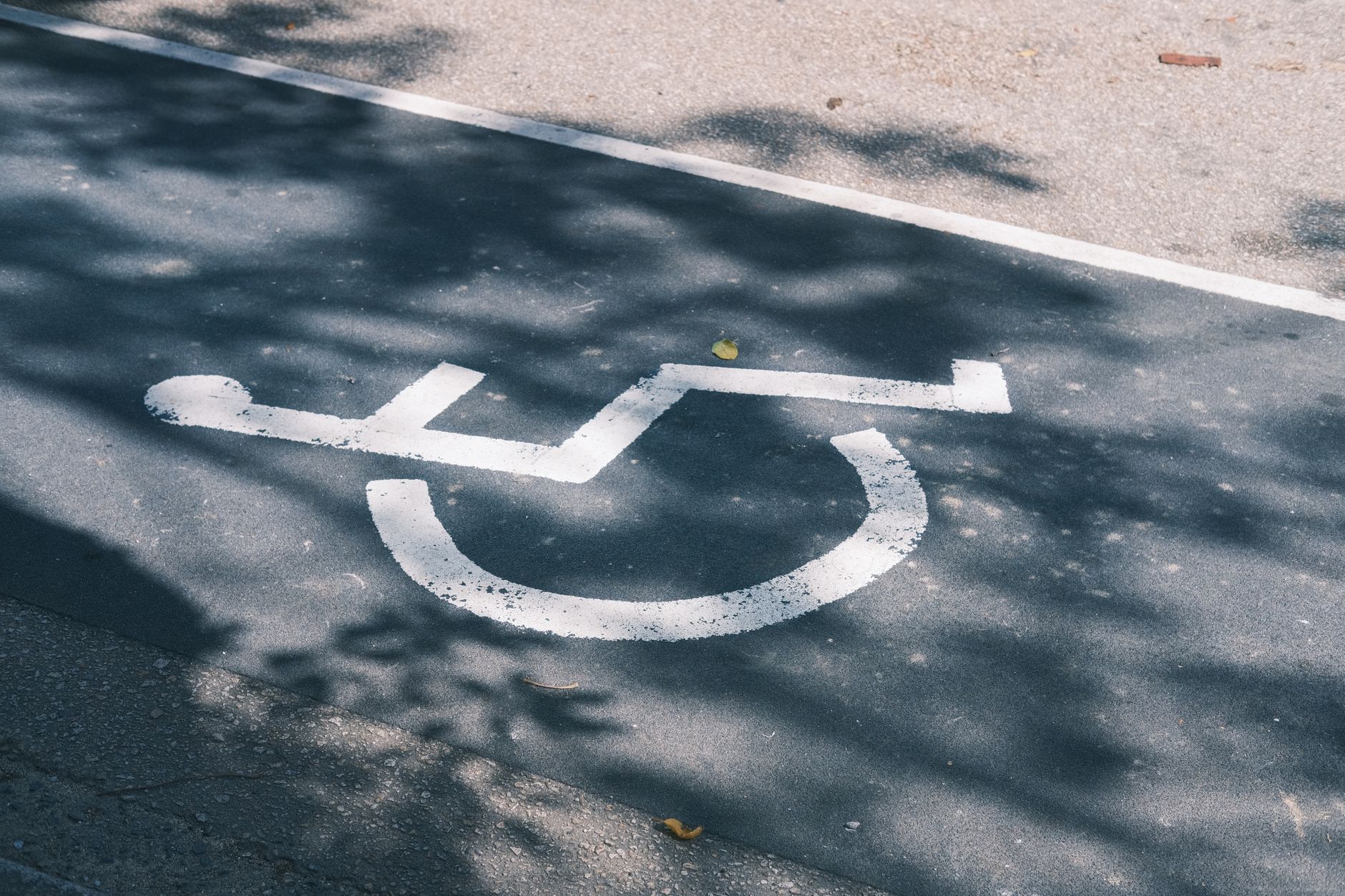 Close-up of an accessible parking symbol on a sunlit asphalt road.