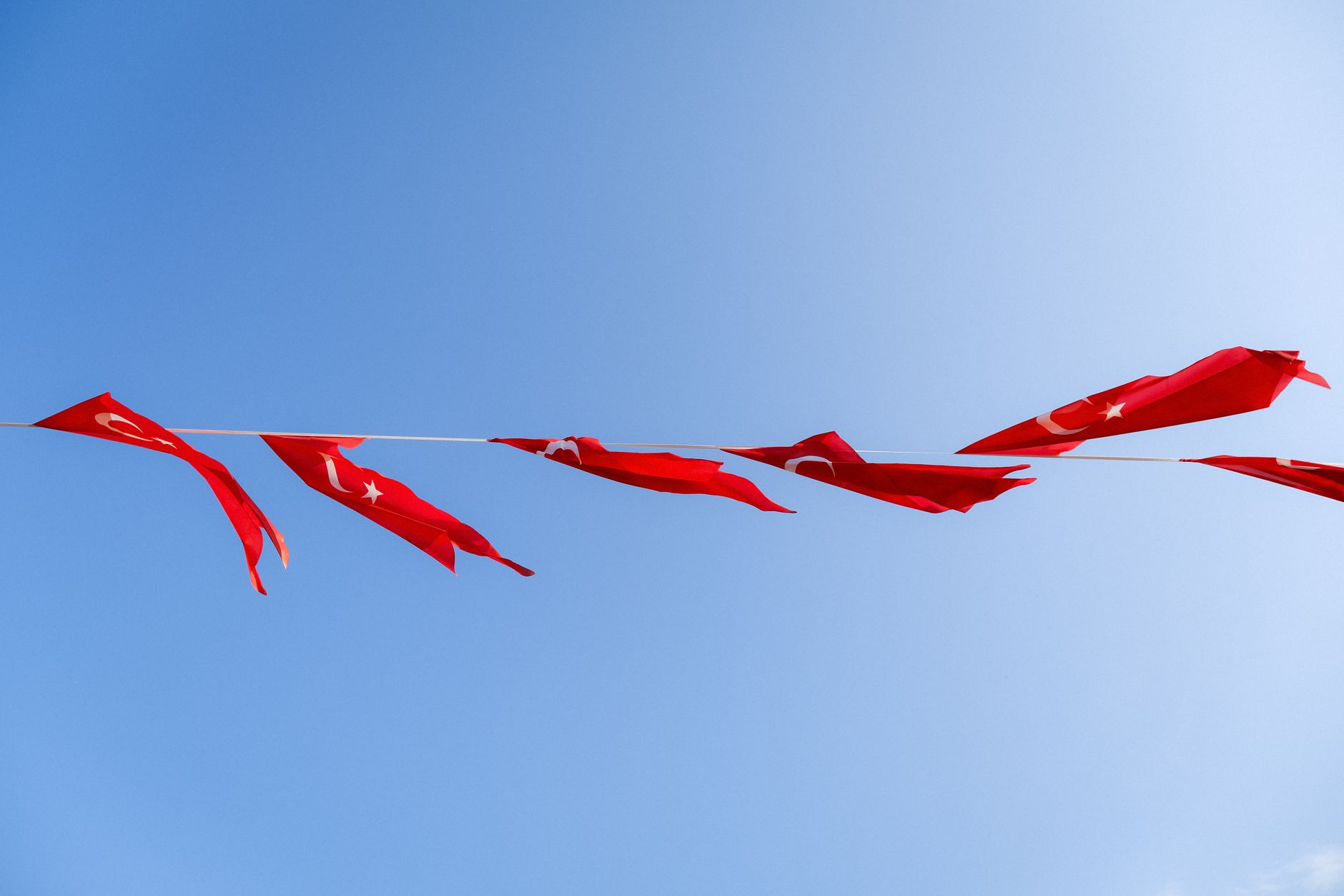 Red Turkish flags flutter on a line against a clear blue sky, symbolizing national pride and freedom.