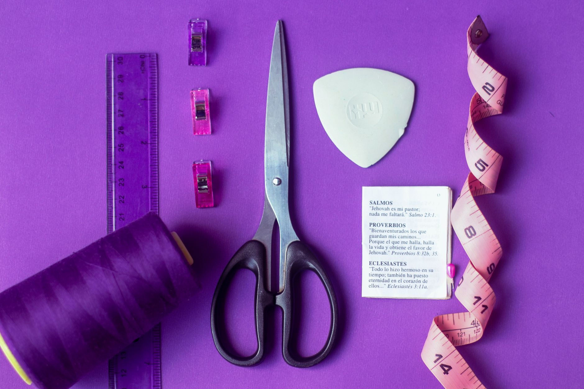 Flat lay of sewing tools including scissors, tape measure, and thread on purple backdrop.