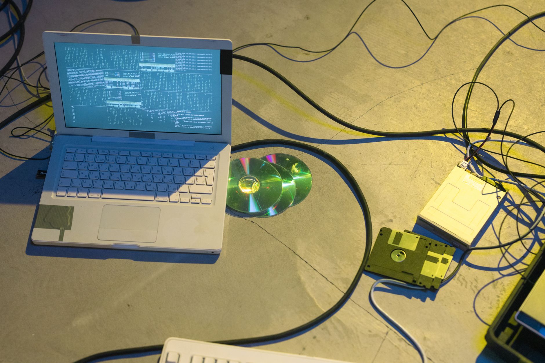 An overhead view of a vintage electronics setup featuring a laptop and disks with tangled cables.