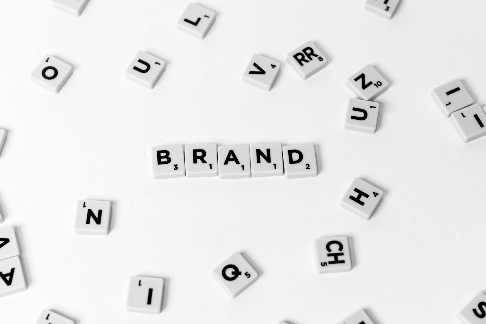 A flat lay of scattered letter tiles forming the word 'BRAND' on a white background.