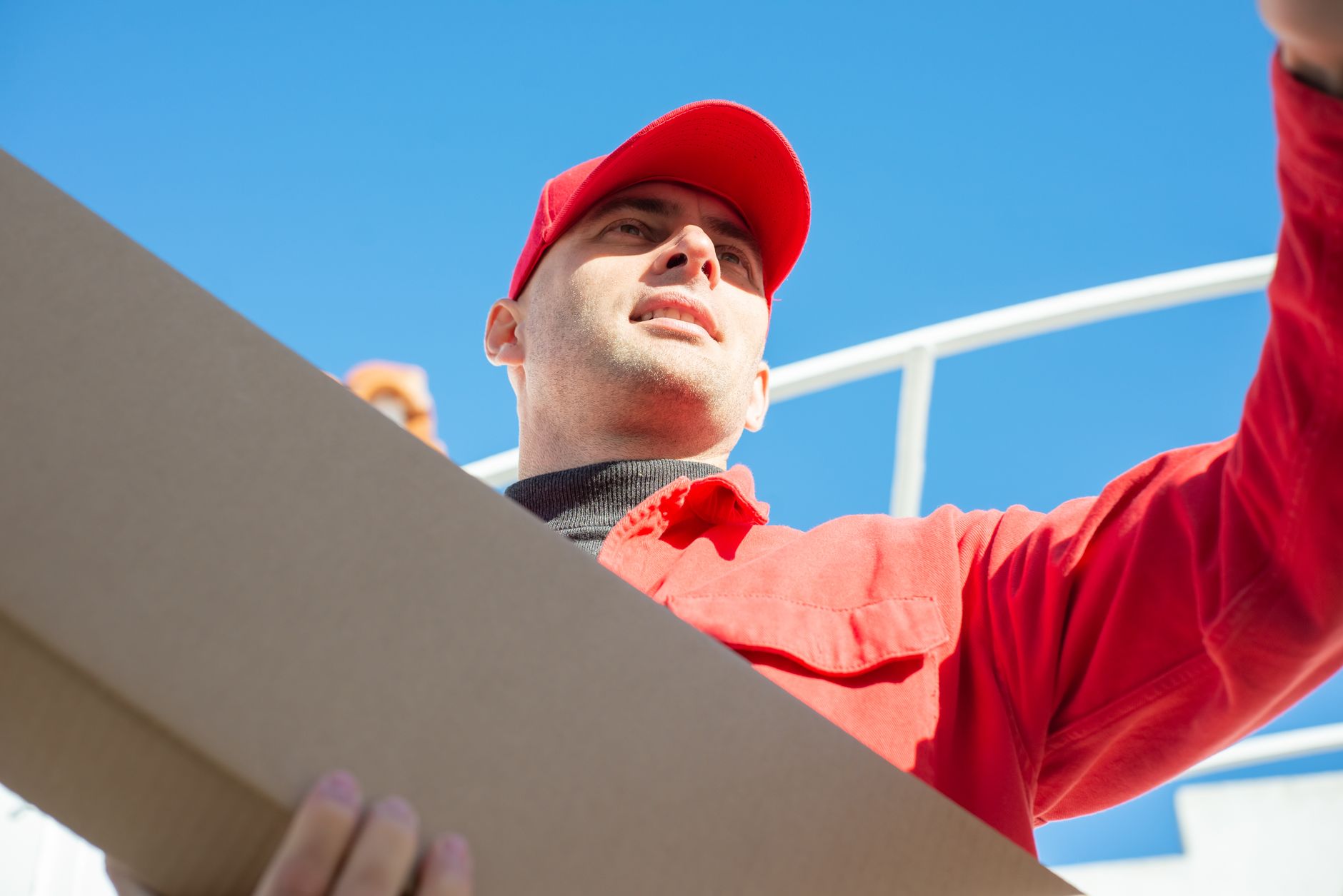 Deliveryman in red uniform delivers package outdoors in daylight.