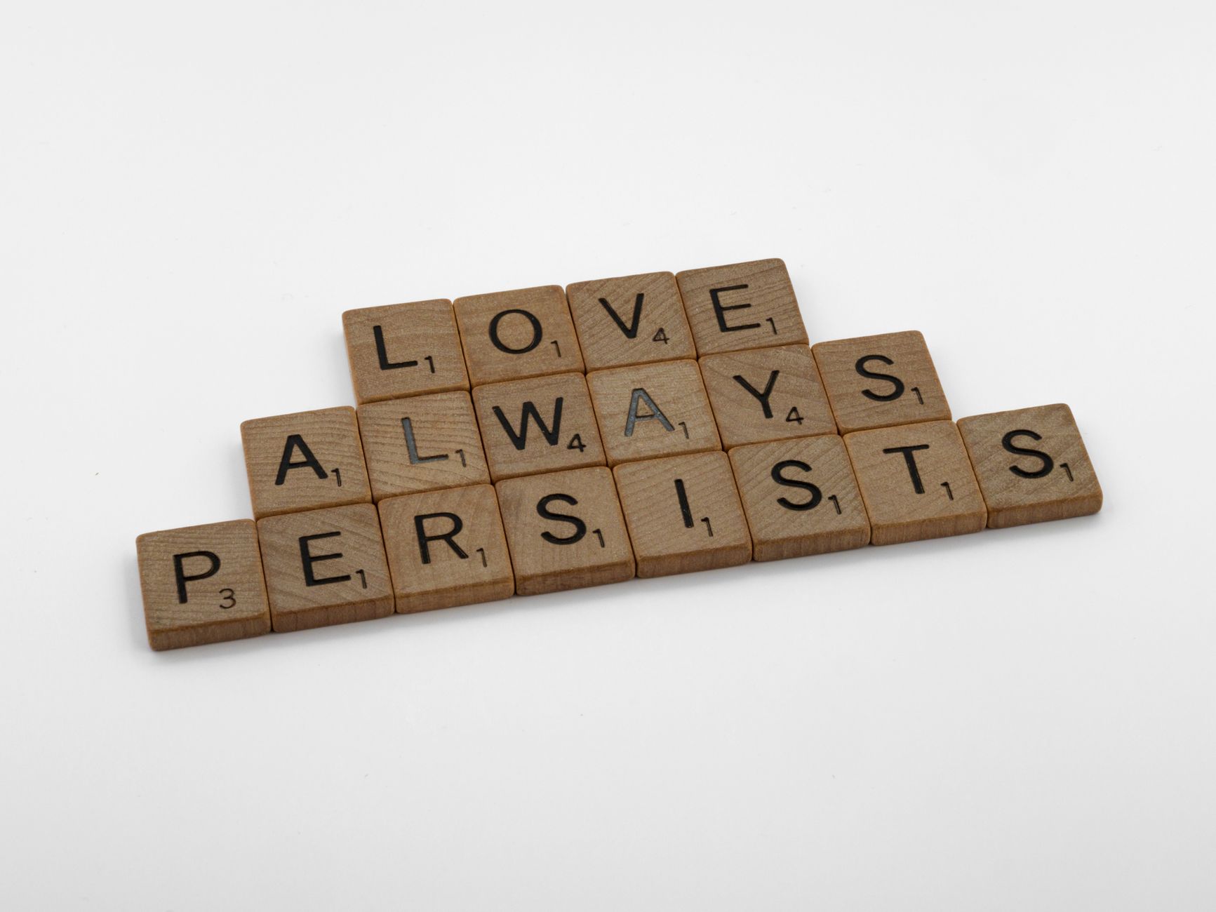 Scrabble tiles on a white background form the phrase 'Love Always Persists', emphasizing a message of enduring love.