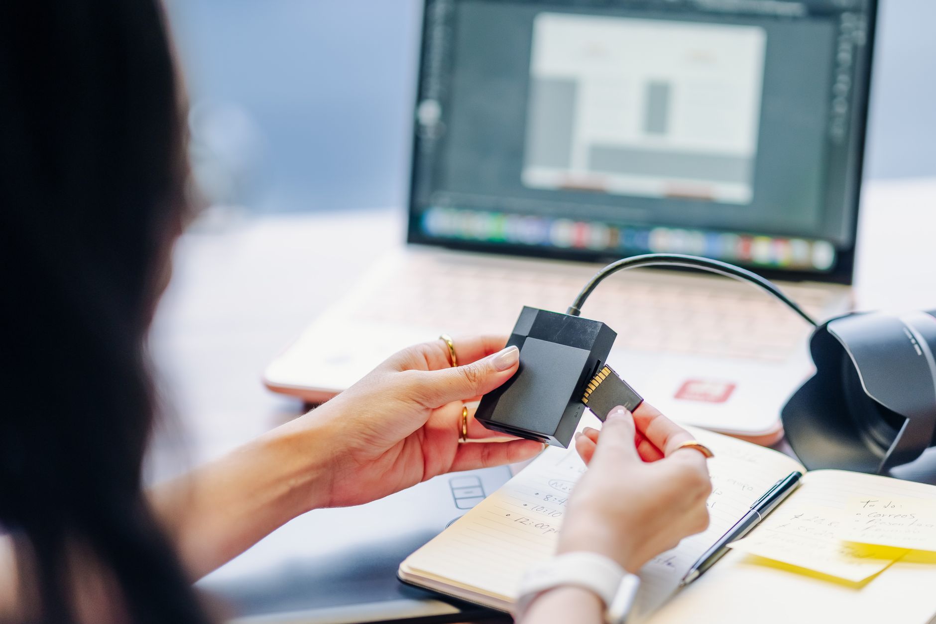 Close-up of hands using a memory card reader connected to a laptop, highlighting digital work essentials.