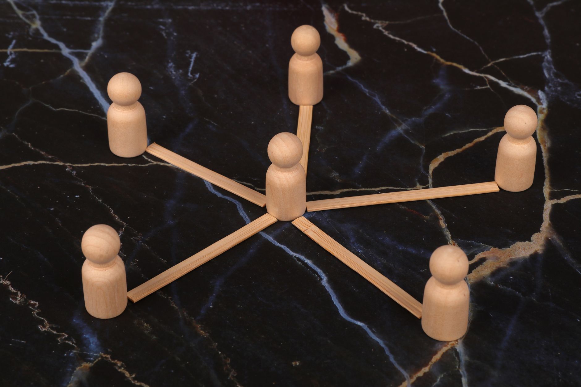 Wooden figures arranged in a network pattern on a marble surface, symbolizing connection or teamwork.