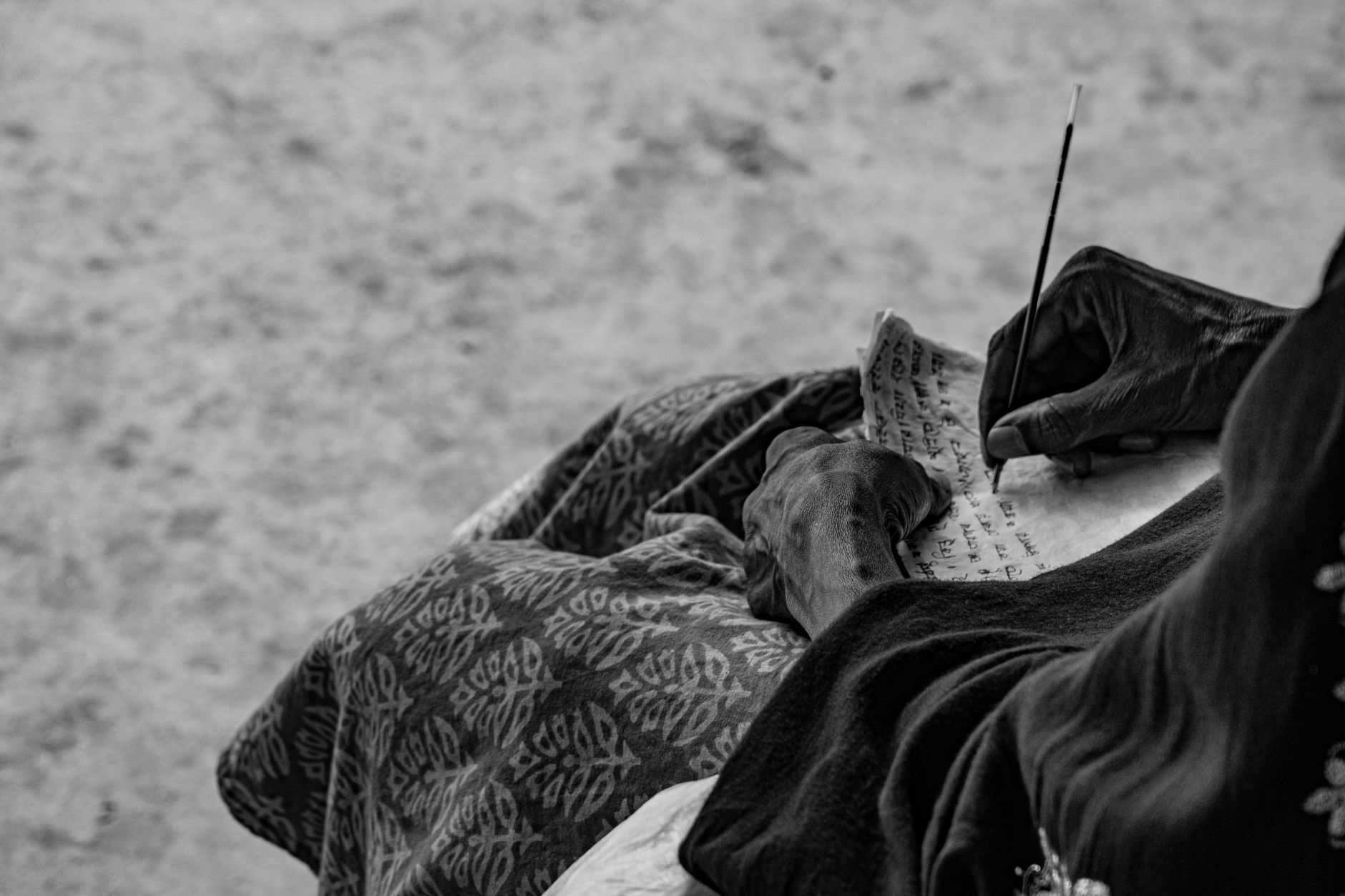 A person engages in writing on paper using traditional ink, captured in black and white.