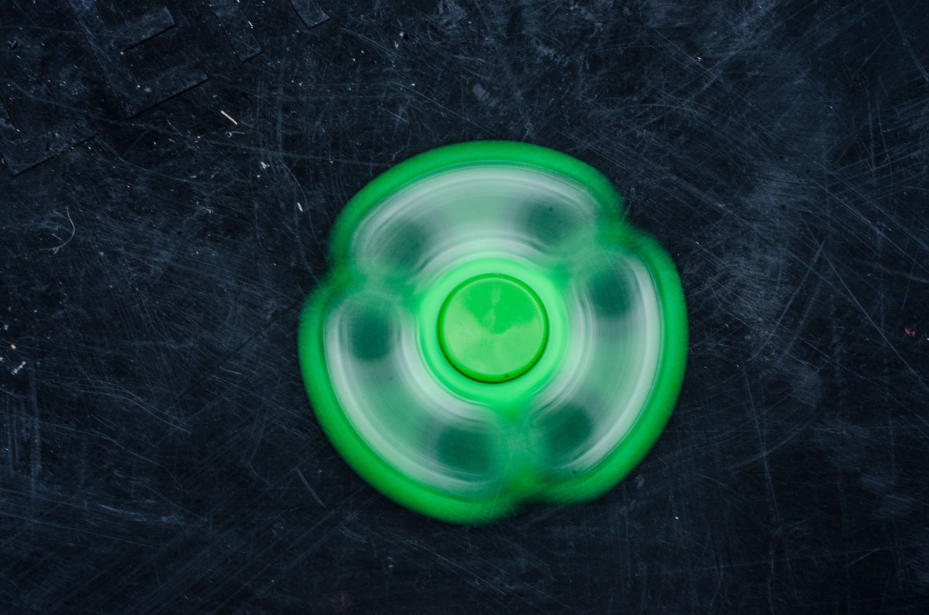 A vibrant green fidget spinner spinning rapidly against a dark textured background.