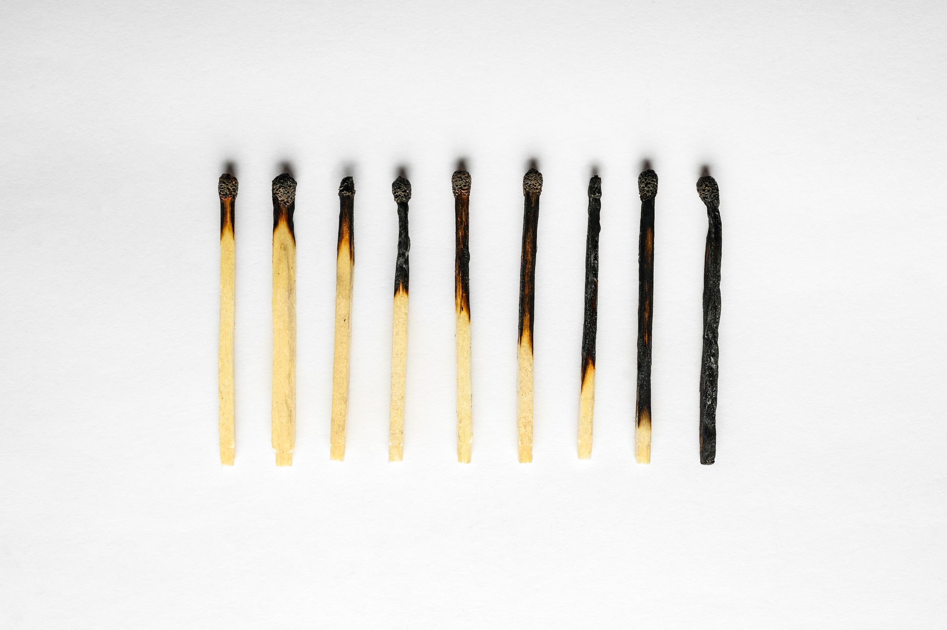 A row of partially burned matches on a white background, displaying a gradient of charring.