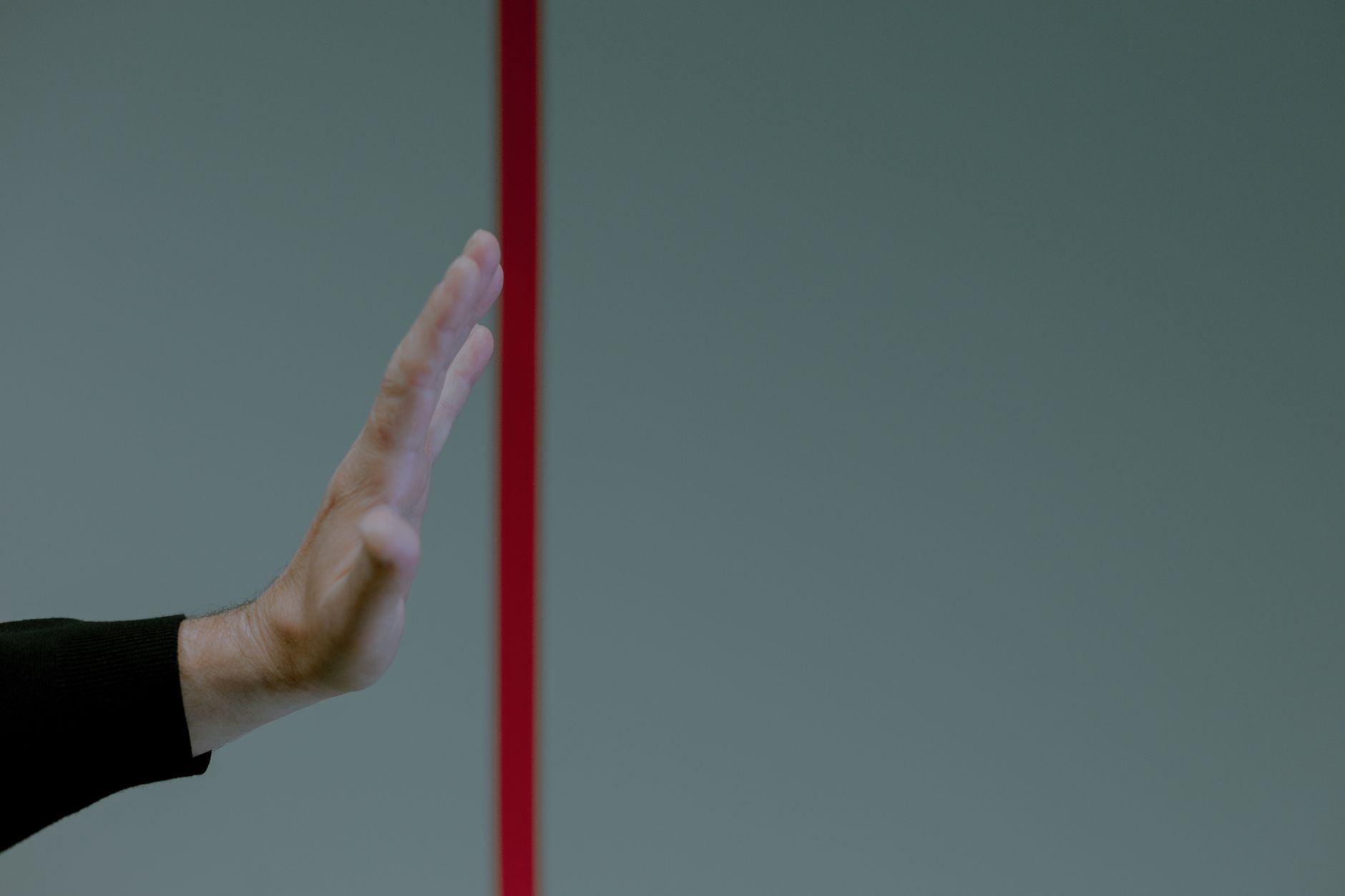 Close-up of a man's hand gesturing stop in front of a vertical red line, concept of boundary.