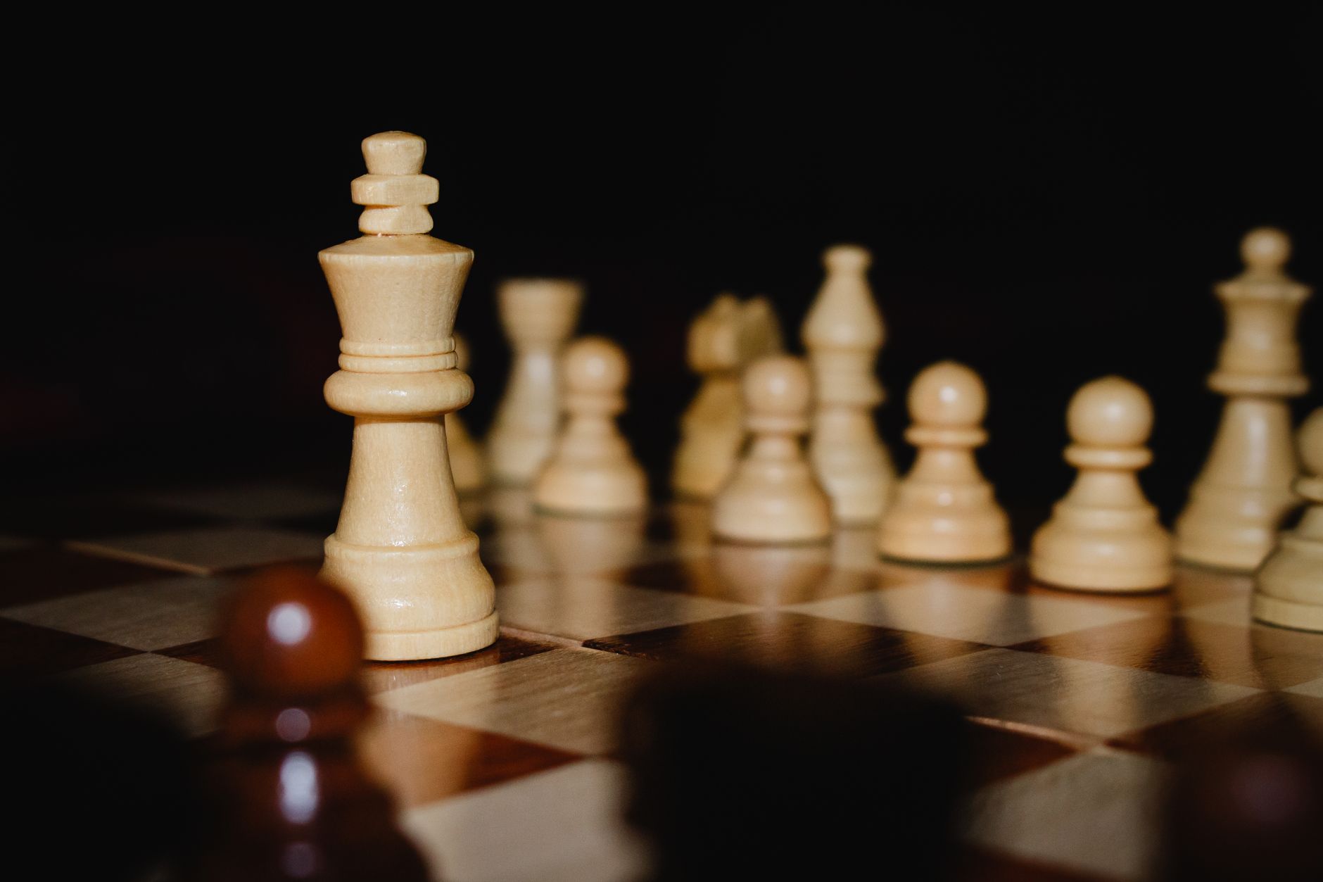 Chess pieces on a wooden board, highlighting the king with a dark background.