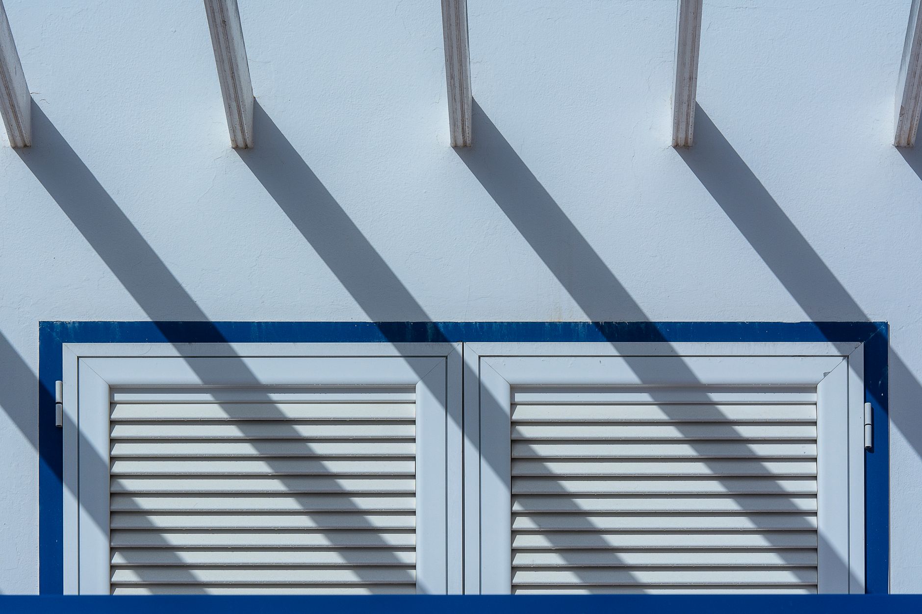 Modern window facade with shutters casting geometric shadows under a clear sky.