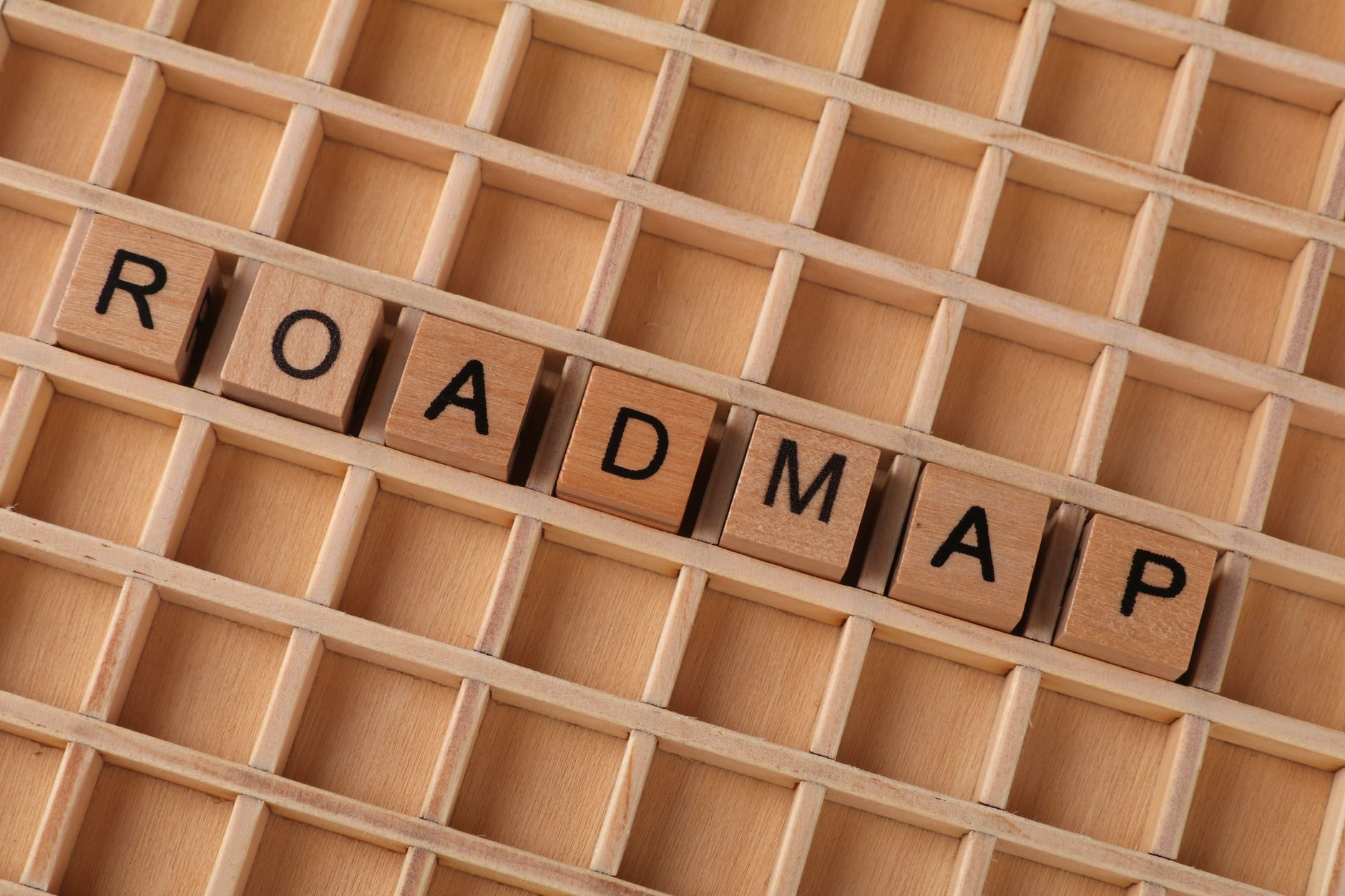 Wooden letter blocks forming the word 'ROADMAP' on a wooden grid background.