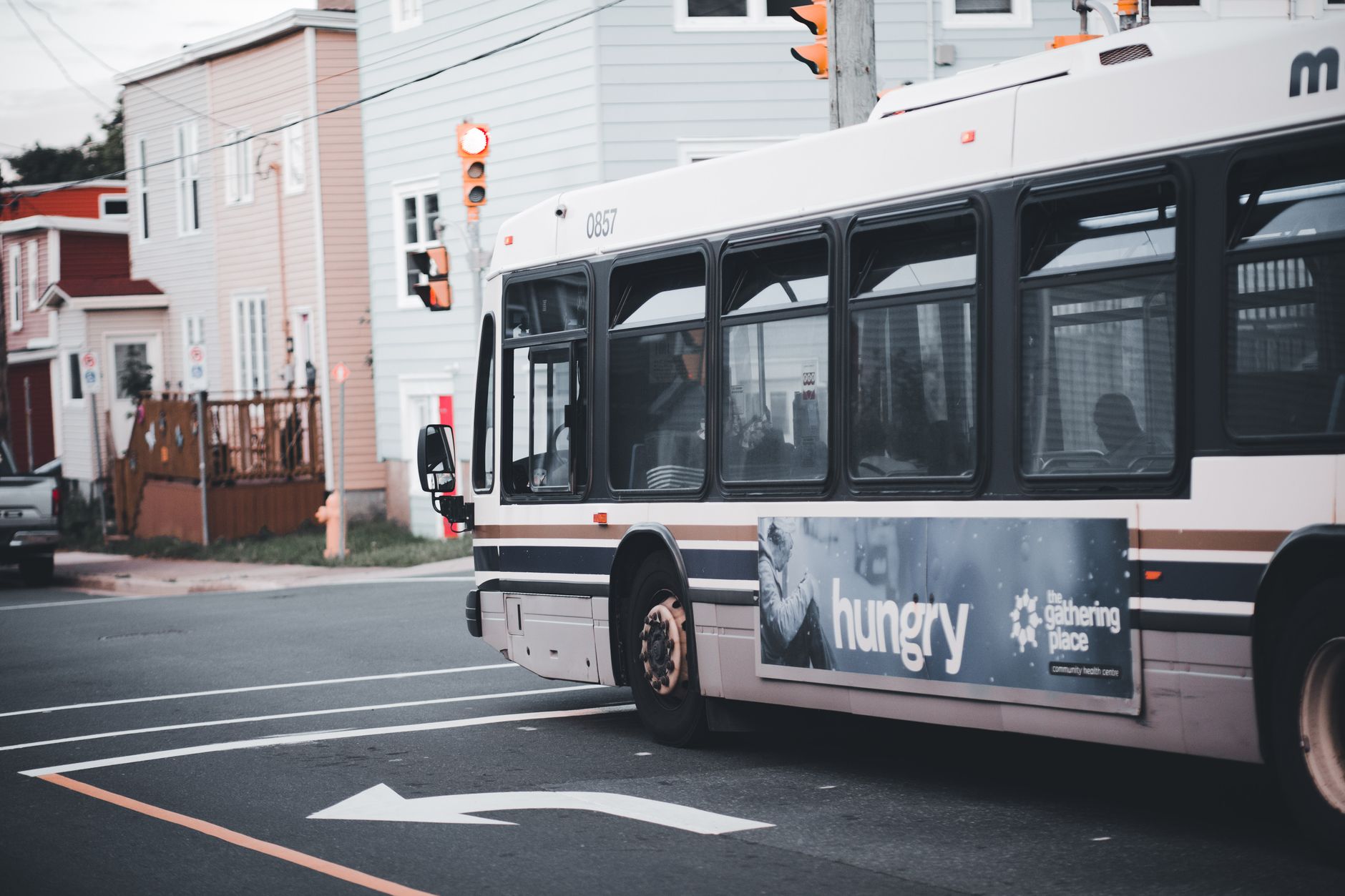 City bus making a turn at an urban intersection with traffic lights and residential buildings.