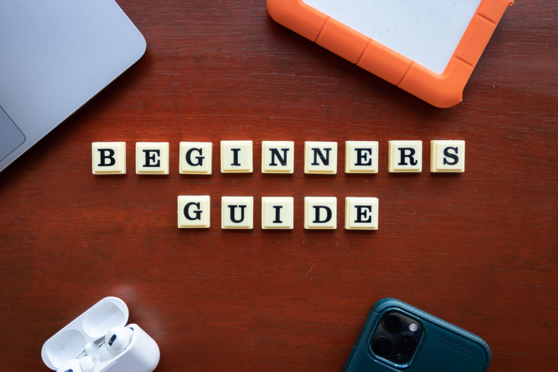 Creative flat lay of gadgets and 'Beginners Guide' text on wooden table.